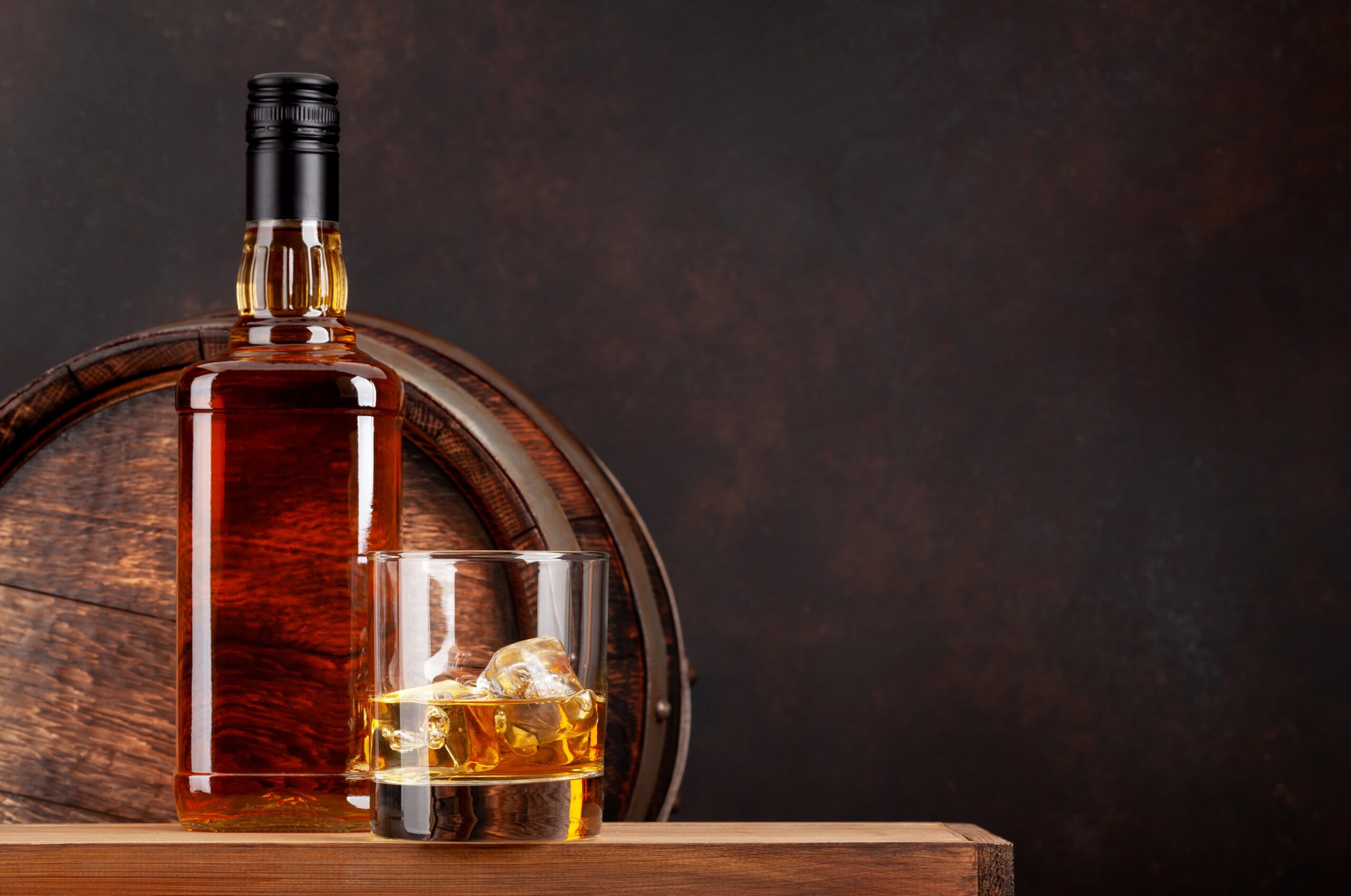front view of whiskey bottle, glass, and old wooden barrel
