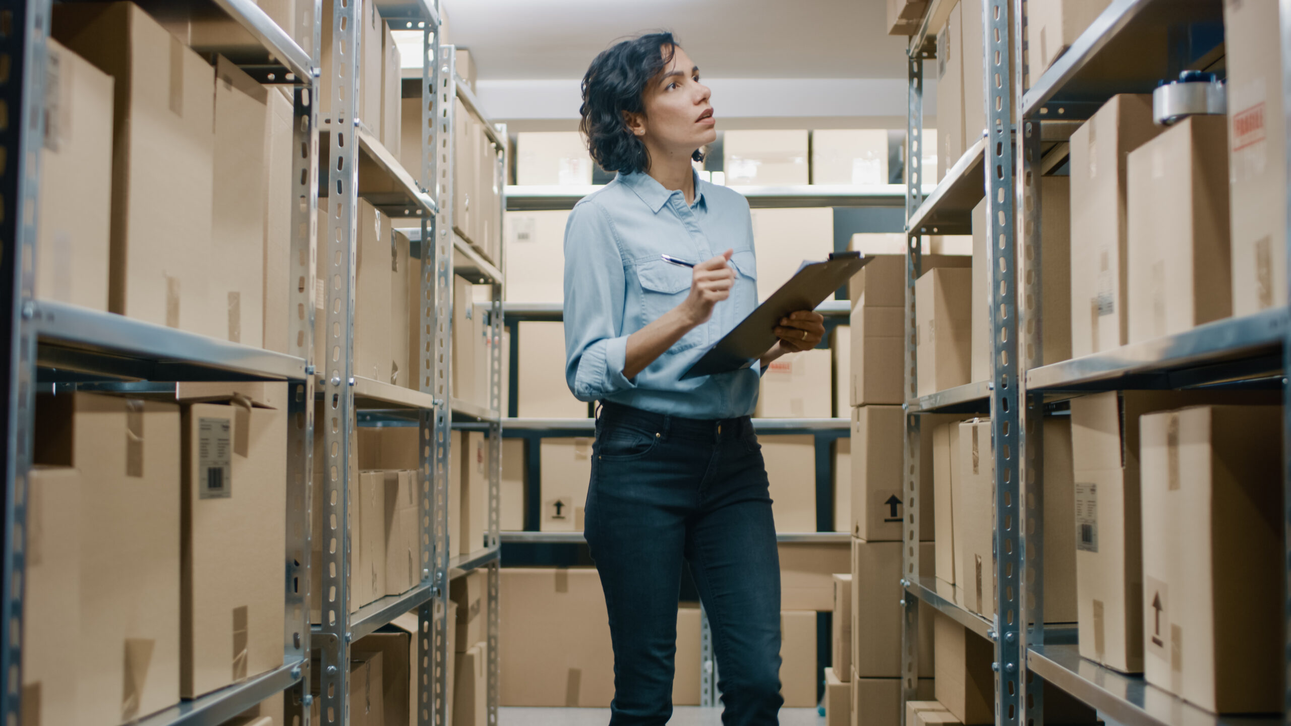 A woman checking inventory in a storage unit full of cardboard boxes